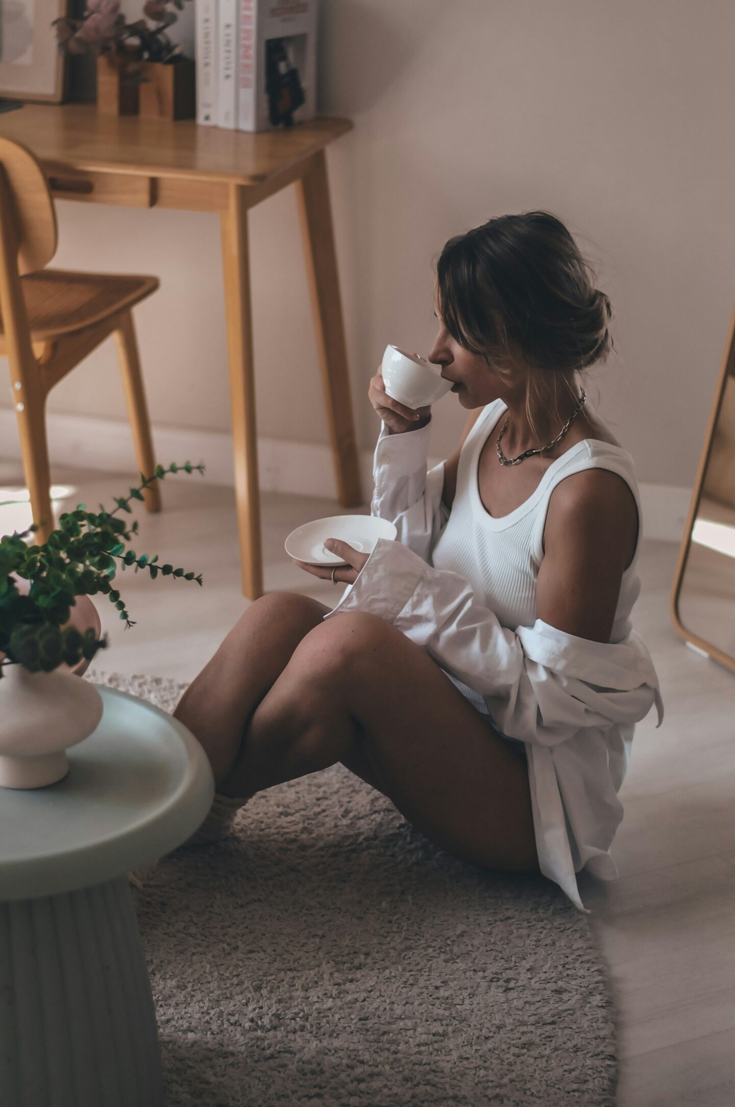 Woman sitting on a rug in a cozy minimalist tidy home, relaxing with a cup of coffee.