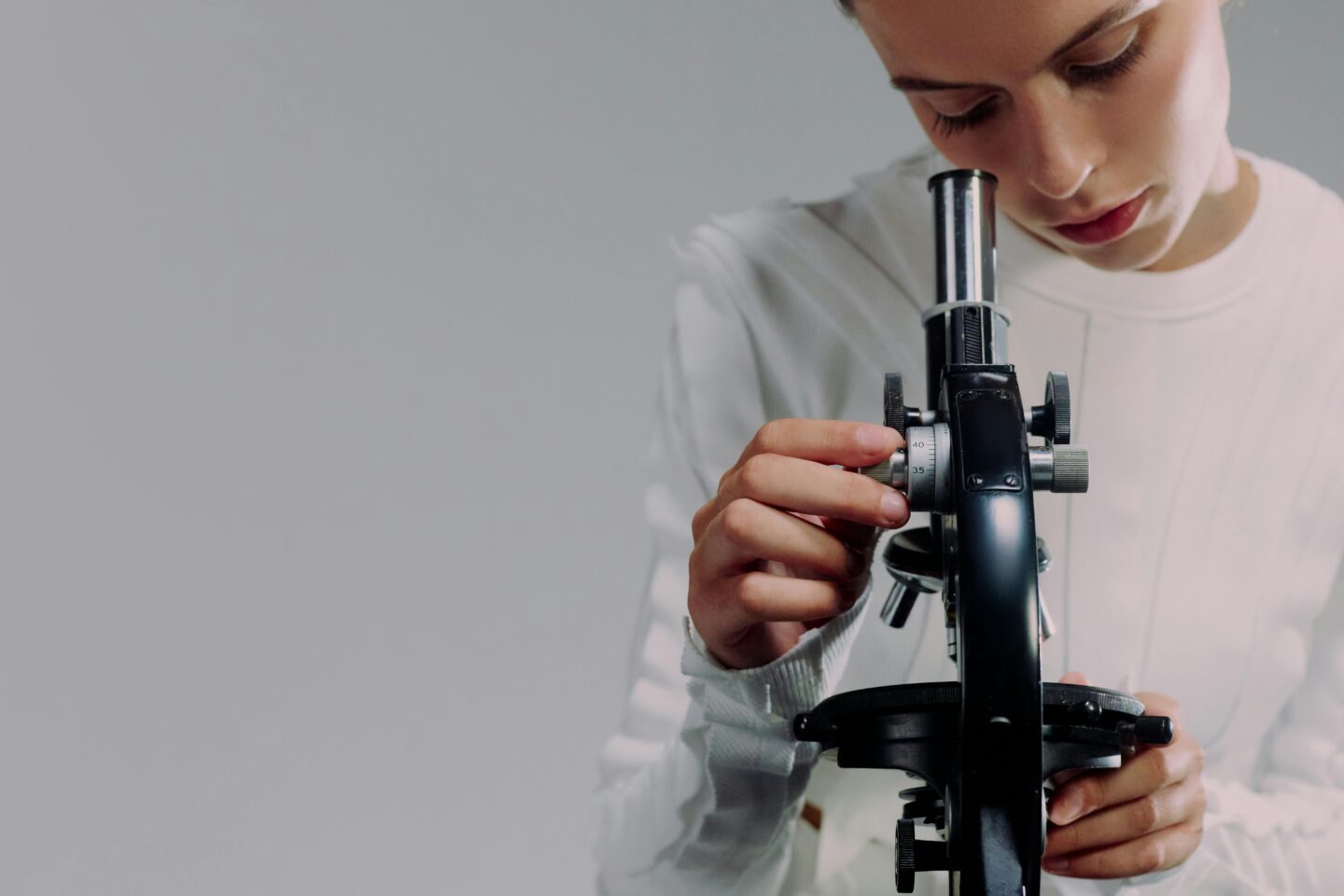 Scientist looking through a microscope and adjusting the focus knob in a laboratory setting.