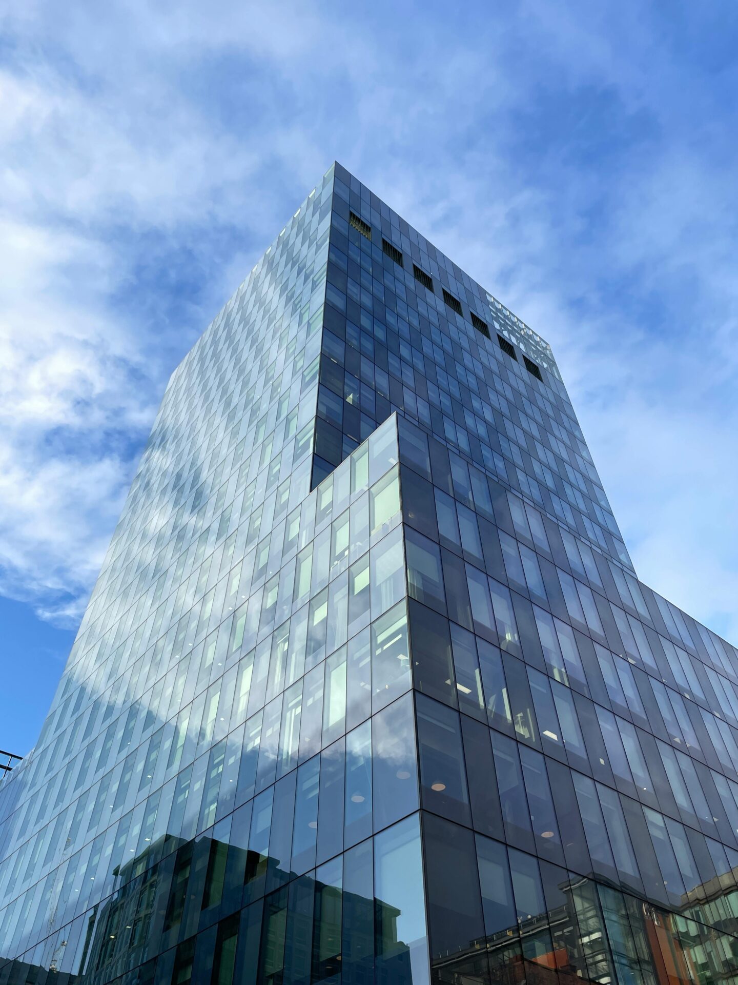 Modern glass commercial building reflecting the blue sky and surrounding architecture, captured from a low angle.