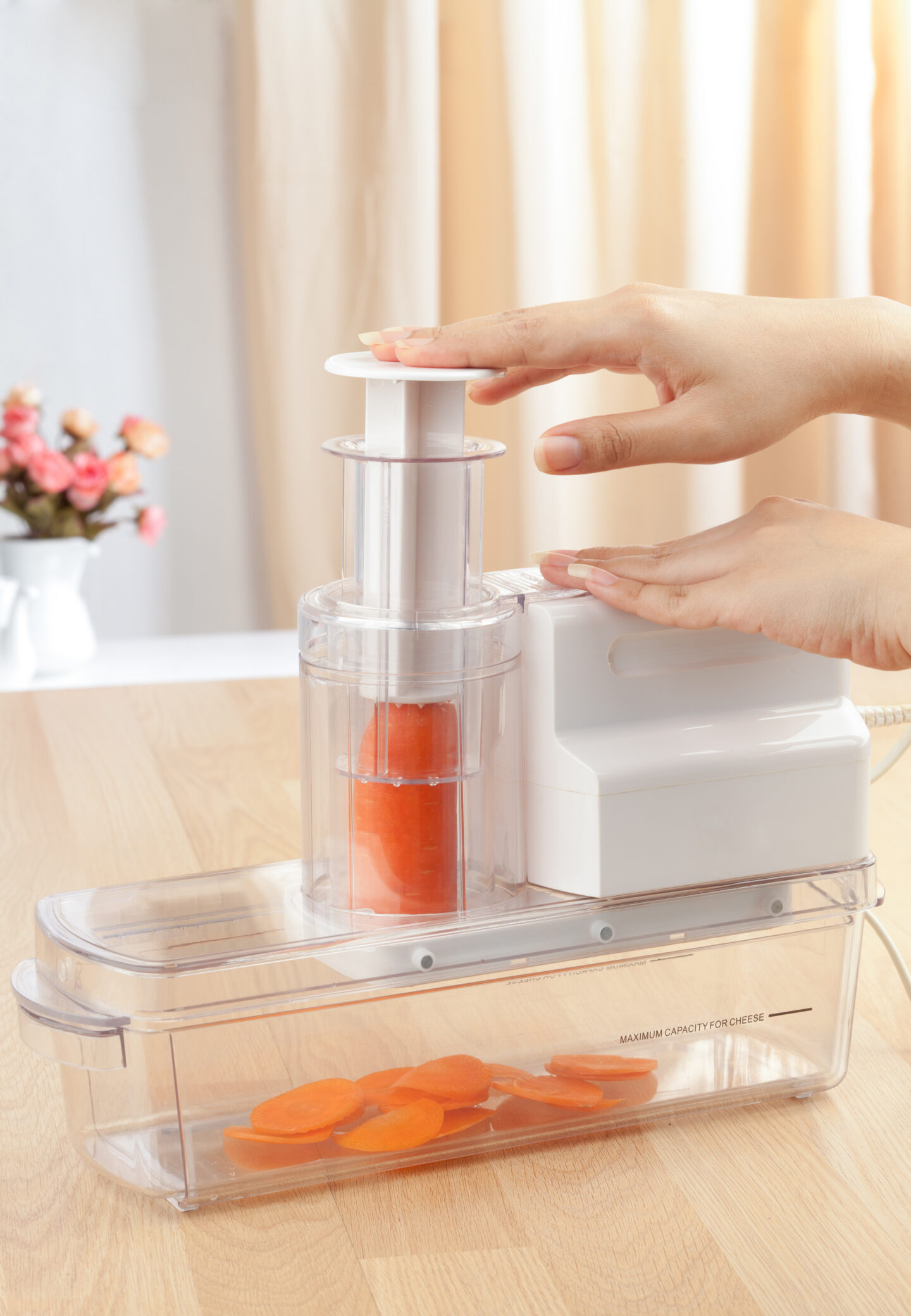 Electric Vegetable Slicer – A kitchen appliance being used to slice a carrot into thin pieces, with slices collected in the container below.