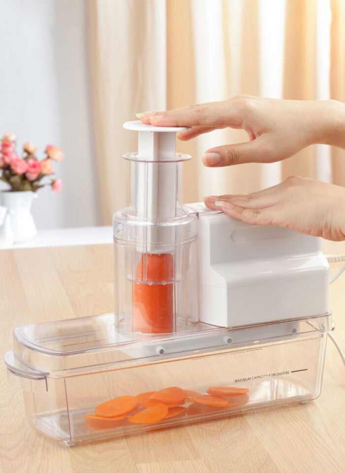 Electric Vegetable Slicer – A kitchen appliance being used to slice a carrot into thin pieces, with slices collected in the container below.