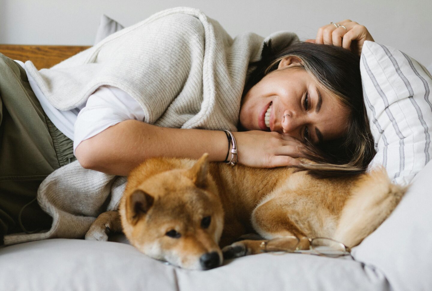 A woman smiling and cuddling with a Shiba Inu dog on a couch.