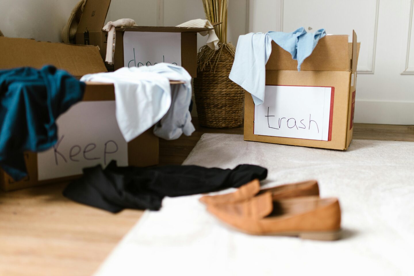 Cardboard boxes labeled “keep,” “donate,” and “trash” filled with clothes during a decluttering session.