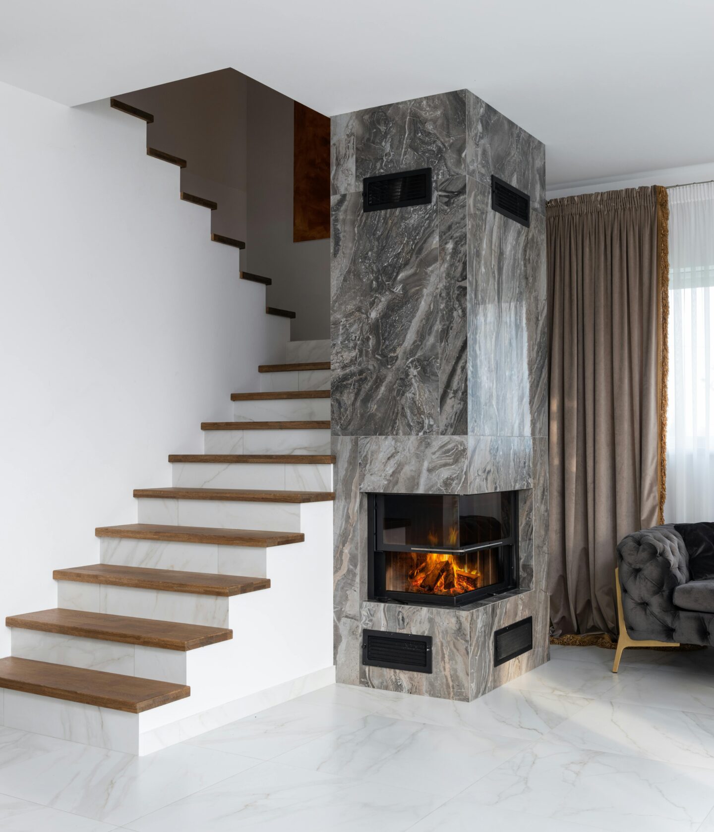 Modern interior with a staircase beside a fireplace, featuring sleek marble look porcelain tiles on the floor and around the fireplace for a luxurious and contemporary design.