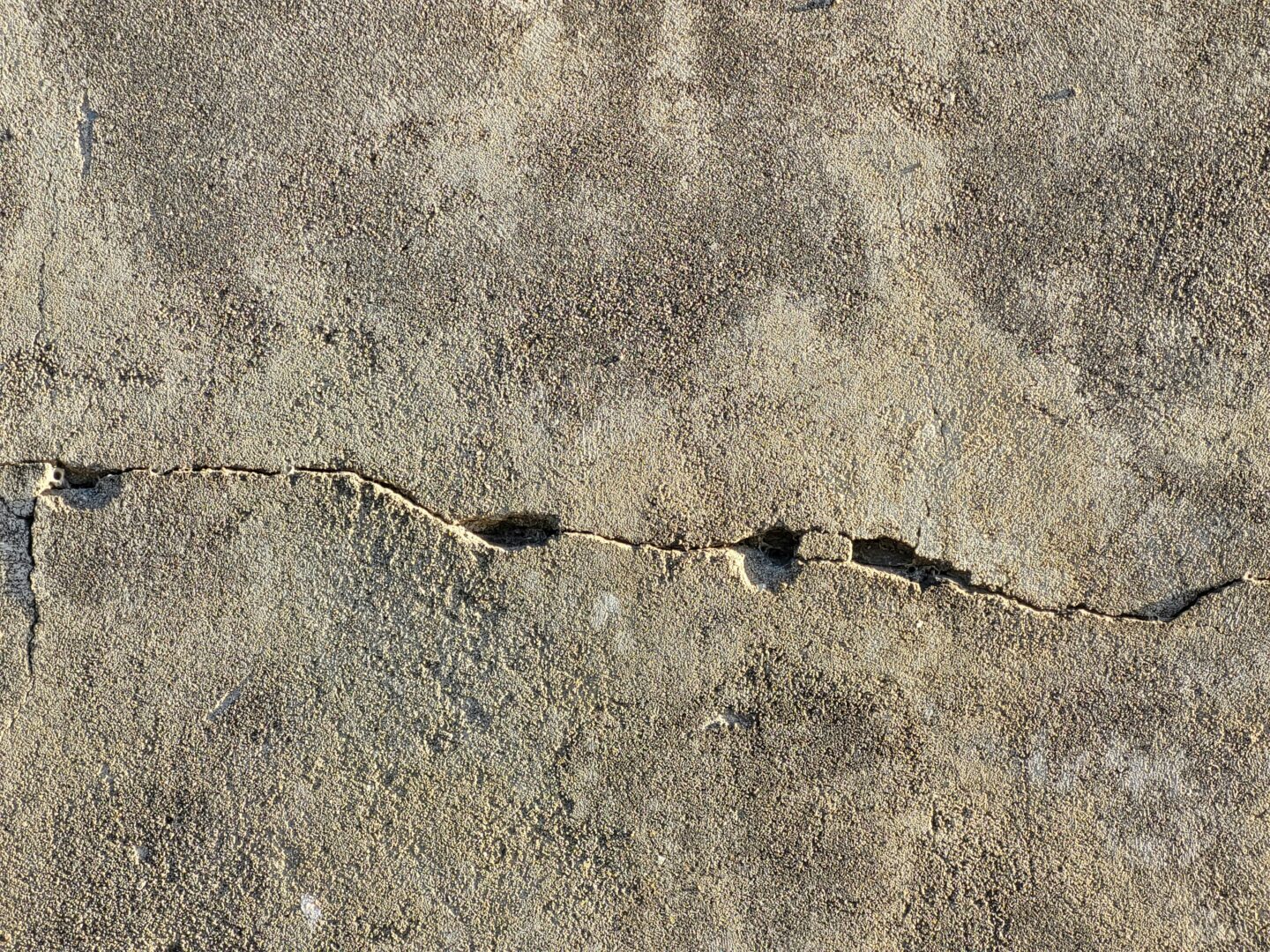 Close-up of a cracked concrete wall with visible texture and uneven surface.