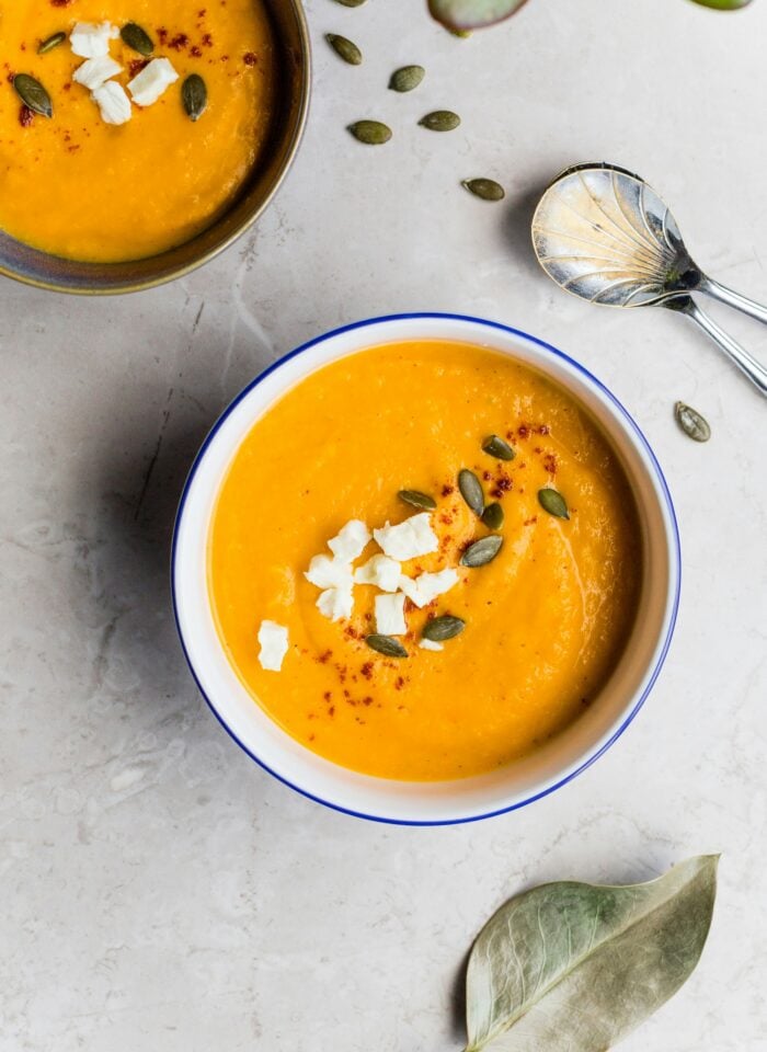 Bowl of creamy pumpkin soup garnished with feta cheese and pumpkin seeds, highlighting winter produce and comforting seasonal flavors.