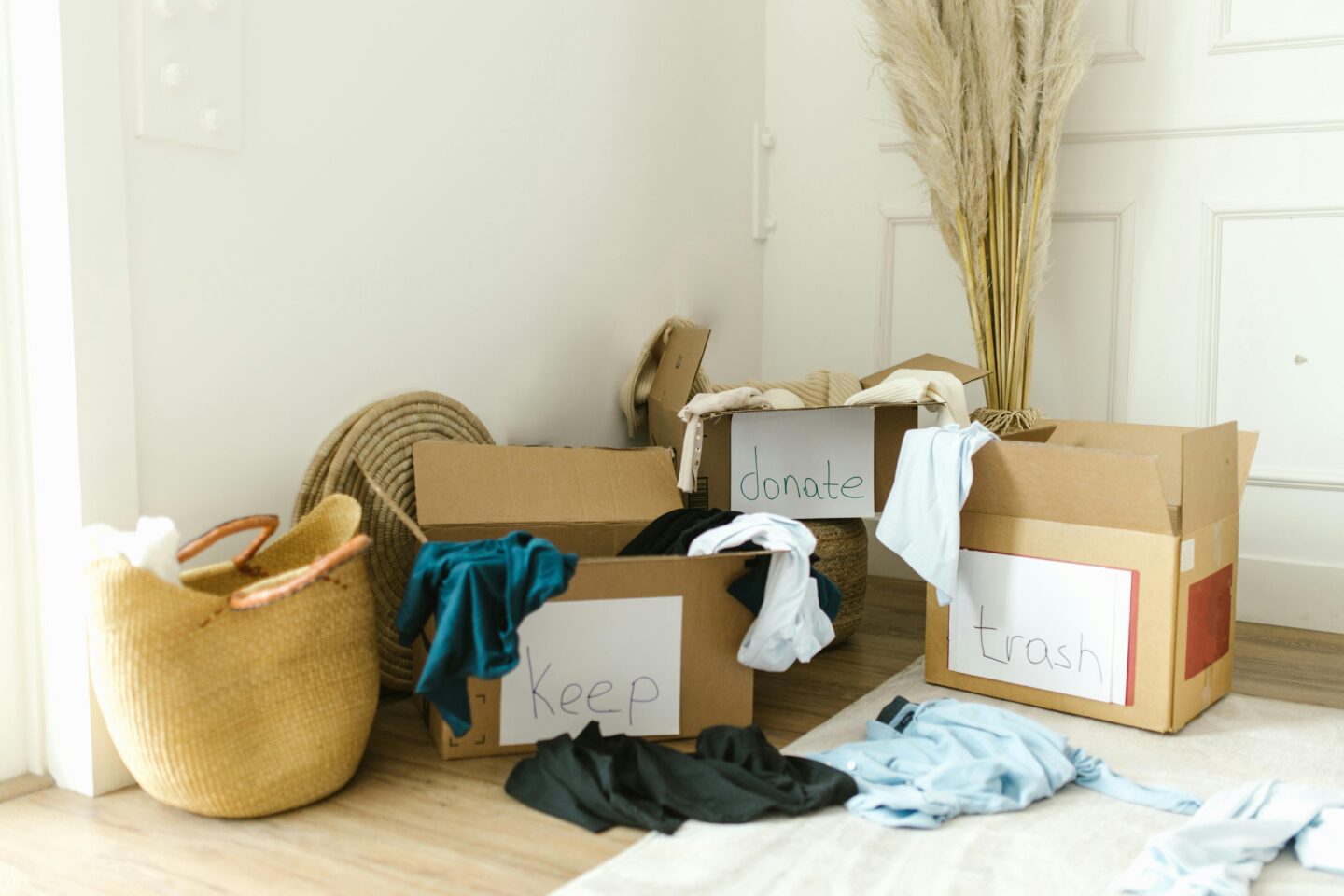 Cardboard boxes labeled “keep,” “donate,” and “trash” filled with clothes during a decluttering and downsizing process.
