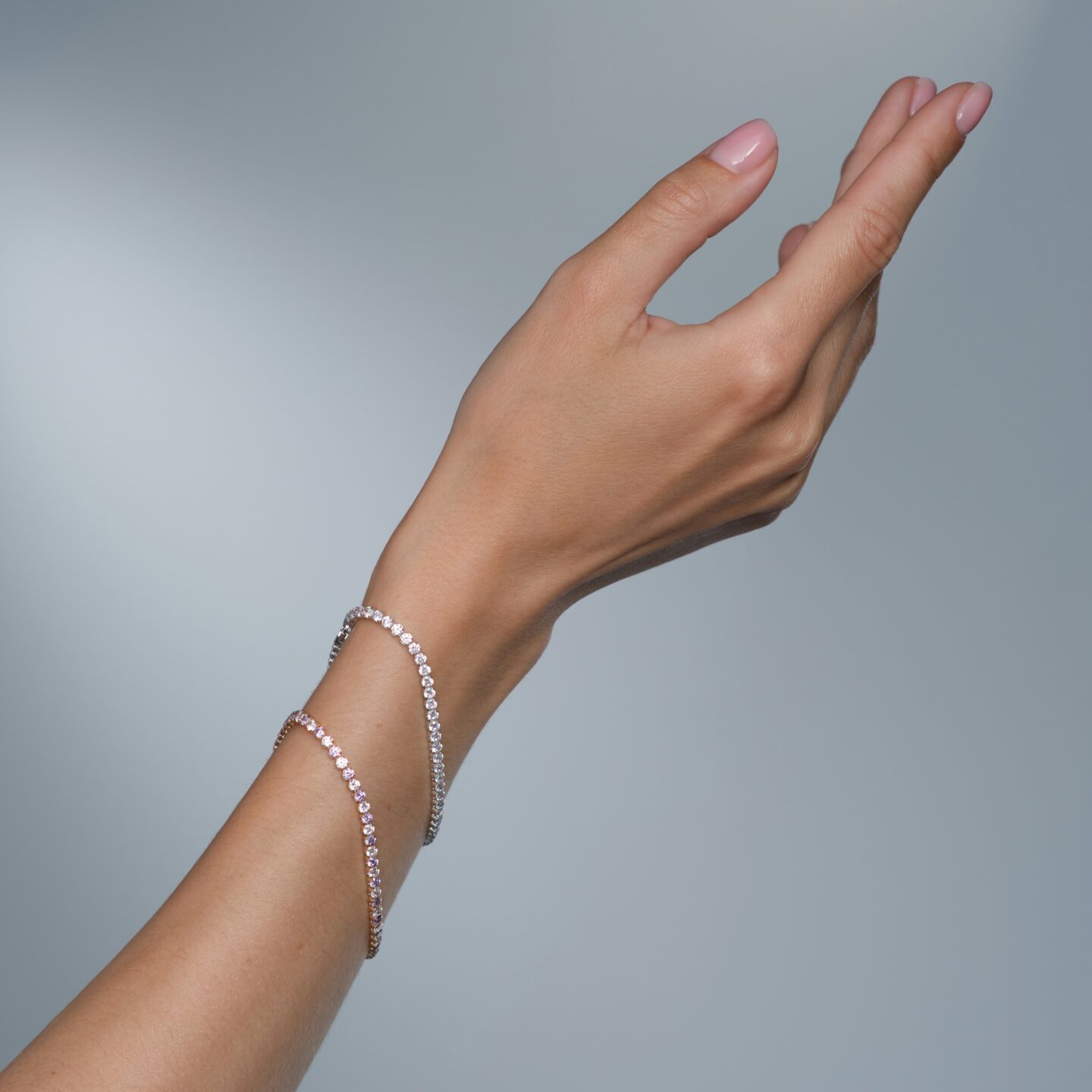Elegant hand adorned with a delicate diamond tennis bracelet, raised gracefully against a soft gray background.