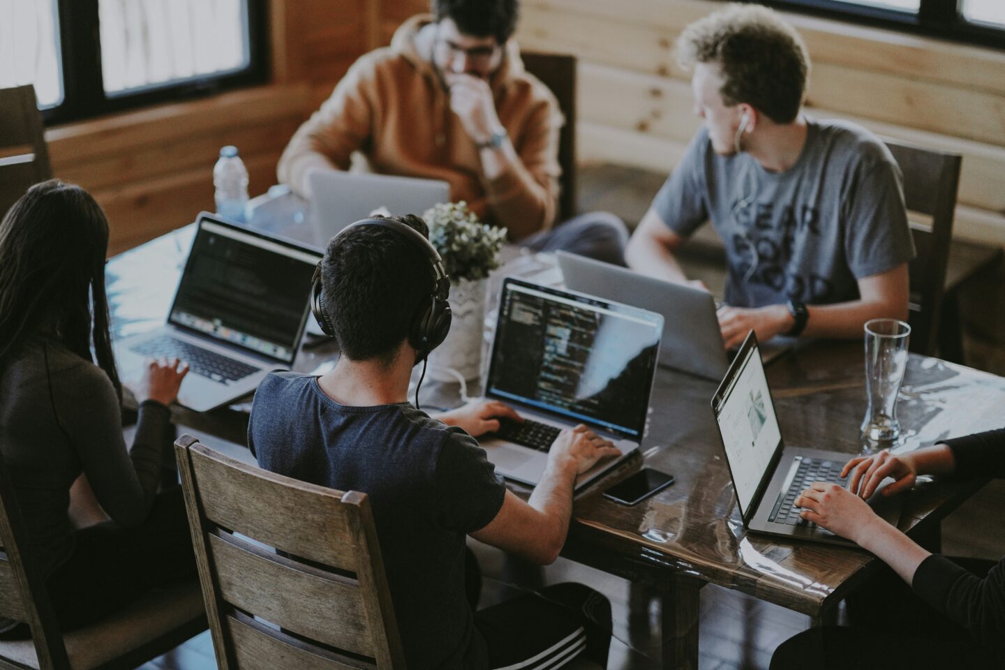Group of young professionals working on laptops in a modern coworking space, collaborating on coding and software development projects.