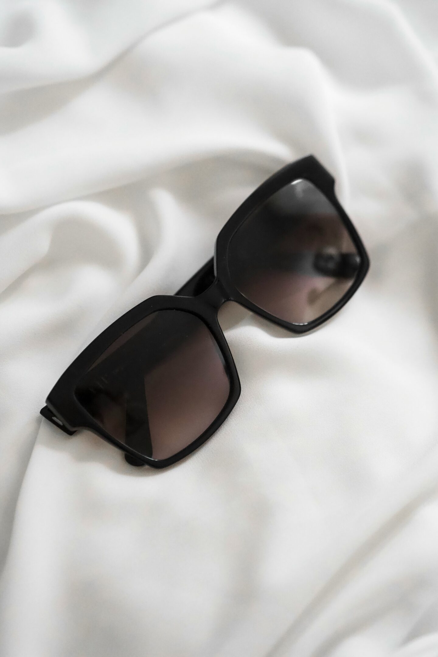 Chic black oversized sunglasses on white fabric — modern luxury accessory for effortless everyday elegance.