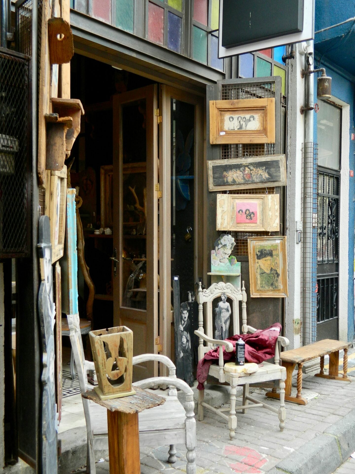 A quirky storefront of a thrift store with antique chairs, wooden frames, and eclectic vintage décor displayed outside.