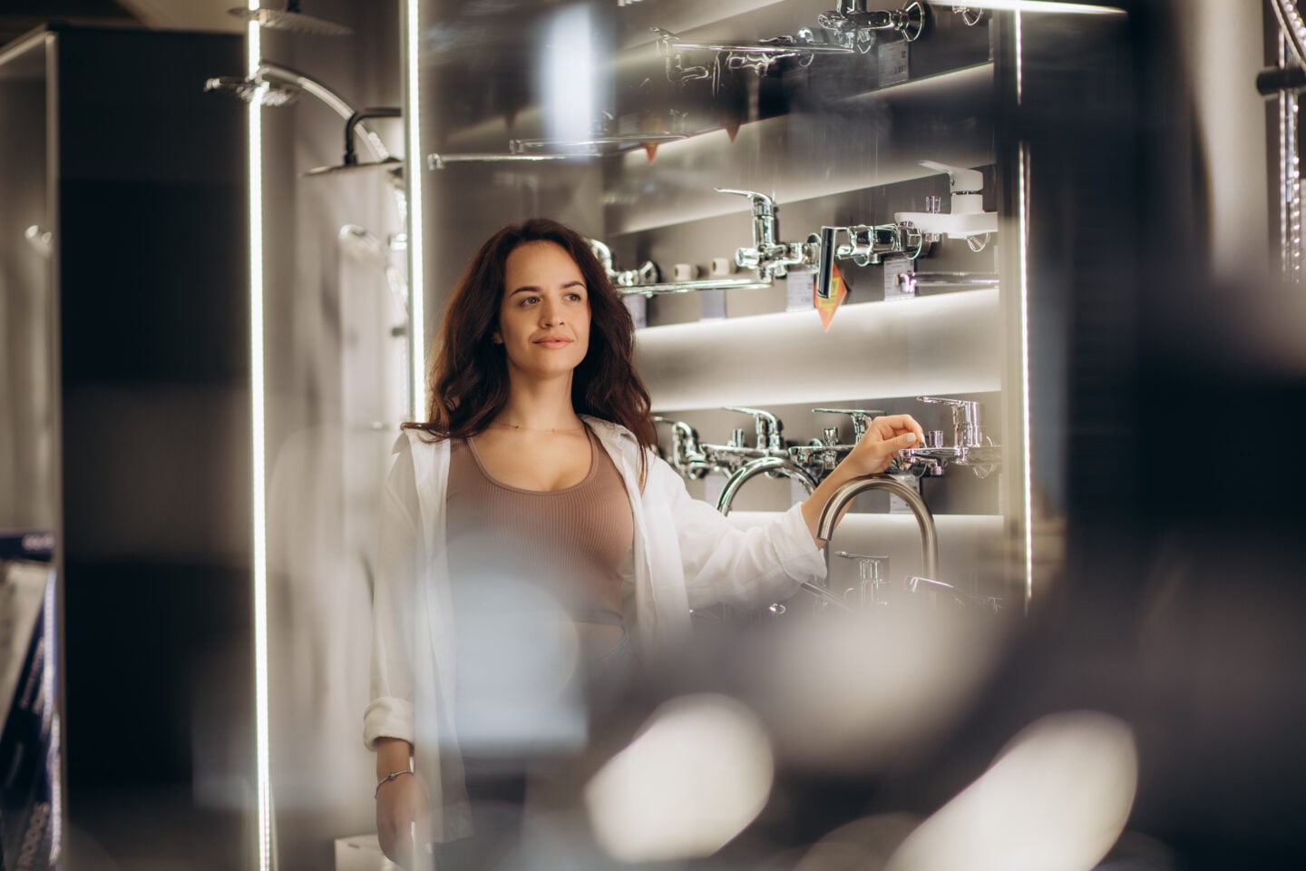 A woman in casual clothes looks at modern faucets and fixtures in a showroom.