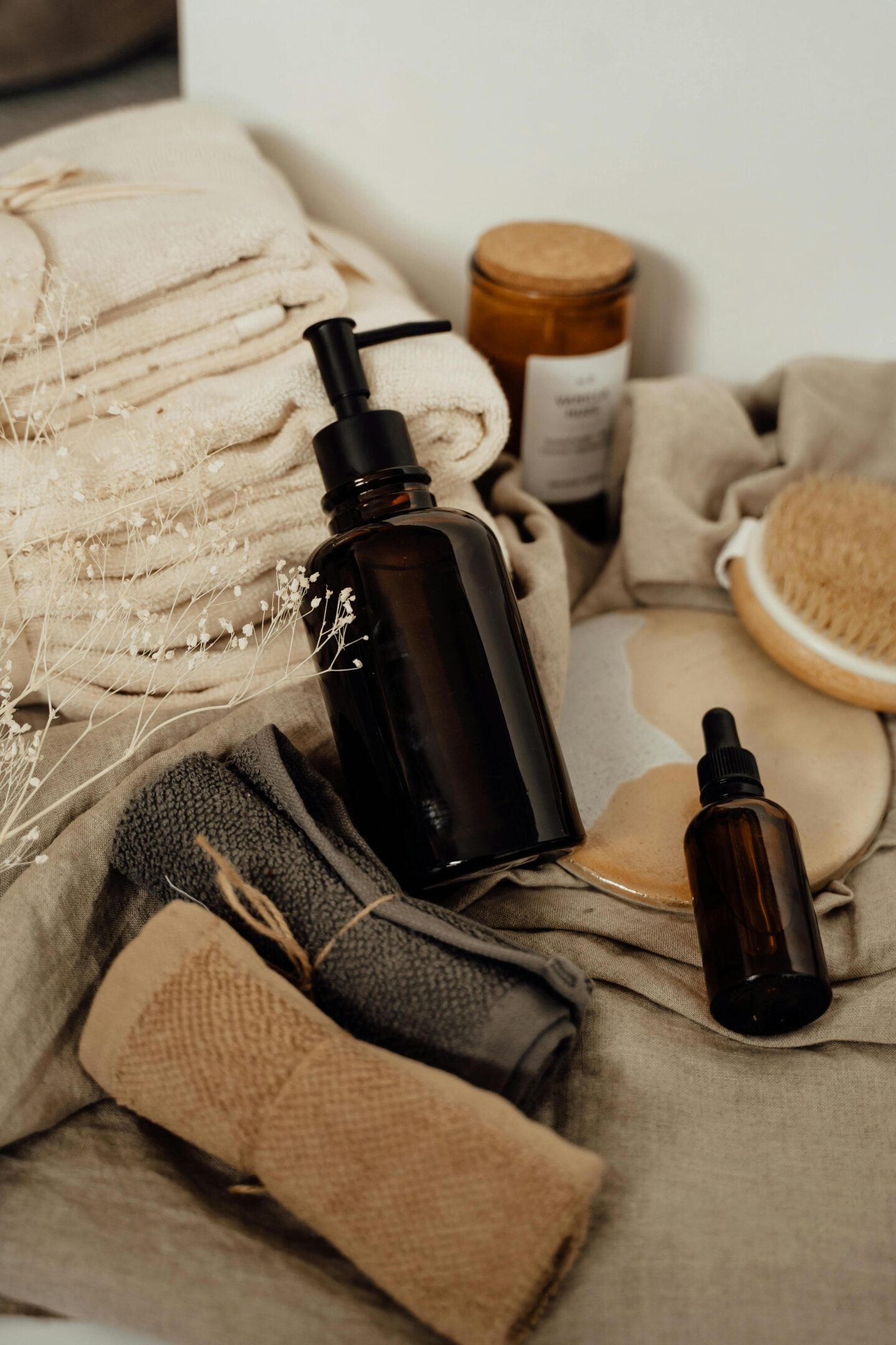 Rolled towels, amber glass bottles, and natural brushes arranged neatly for a spa-like bathroom setting.
