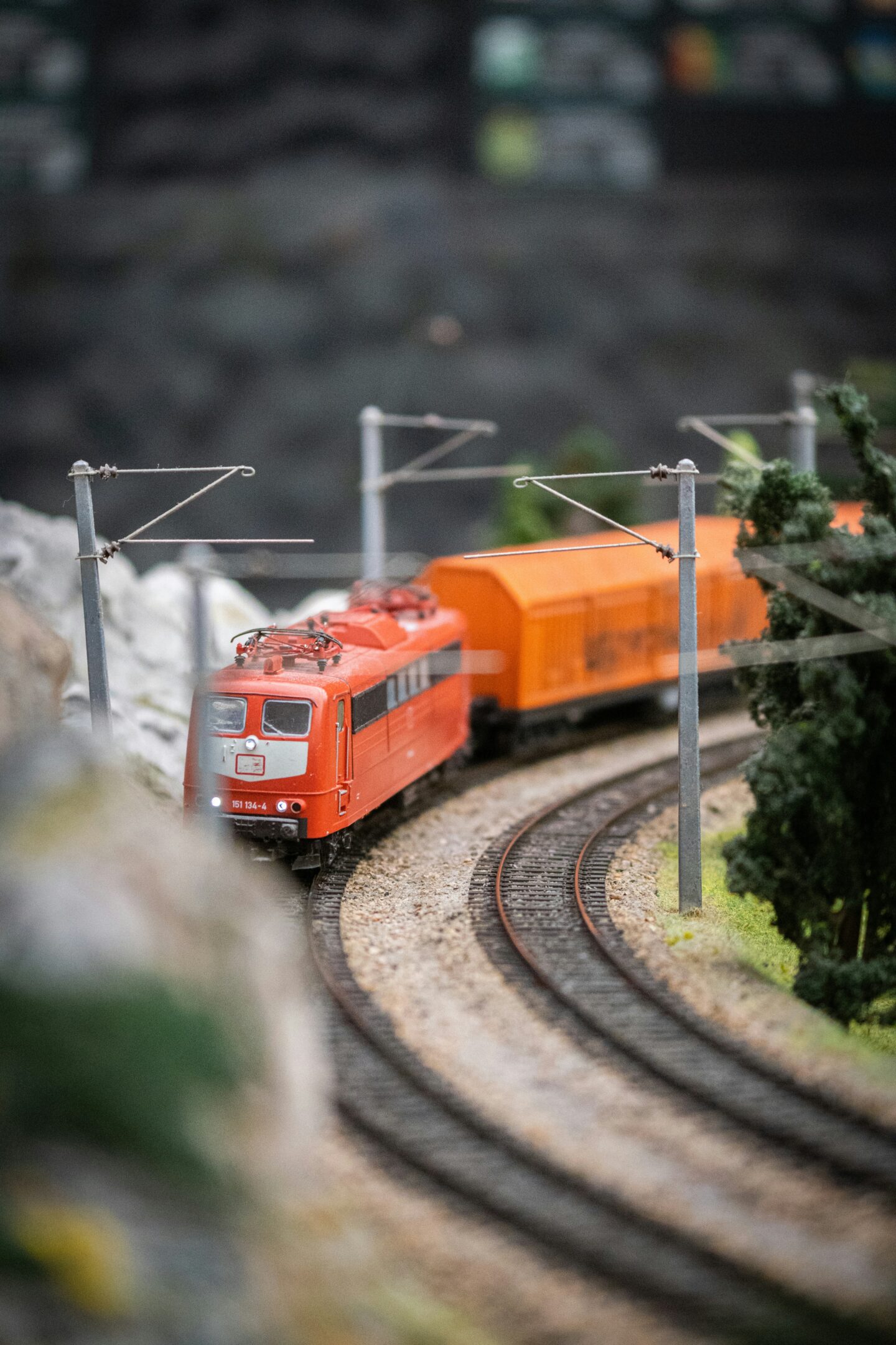Close-up of a miniature model train set with a red locomotive and orange carriages curving along the tracks.