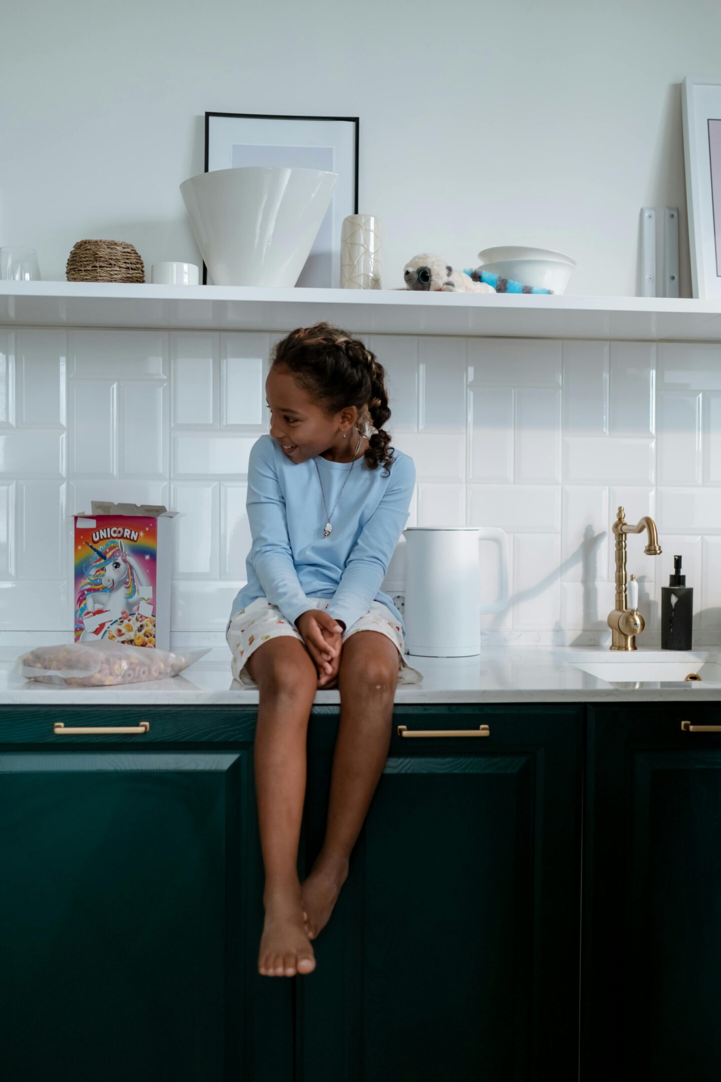 Child sitting on a marble countertop above dark green cabinets with gold handles, emphasizing the high-end cabinet hardware in a bright, modern kitchen setting.