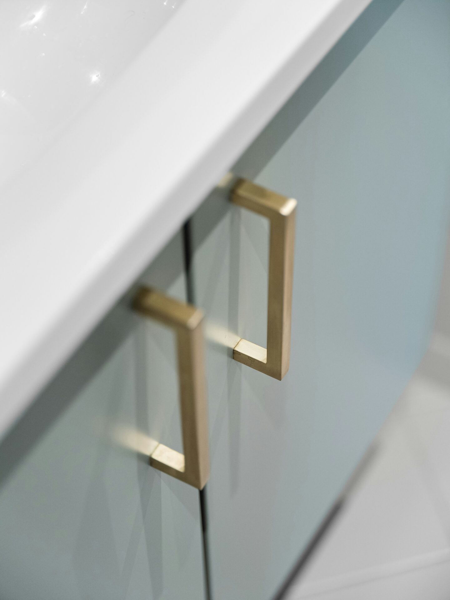 Sleek gold handles on glossy light blue cabinets beneath a white countertop, showcasing a refined and contemporary luxury hardware style.