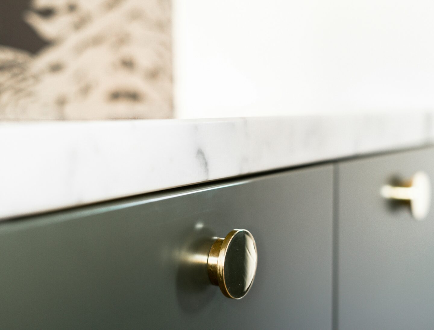 Close-up of elegant gold cabinet knobs on dark green cabinetry with a marble countertop, highlighting the luxurious and modern hardware design.