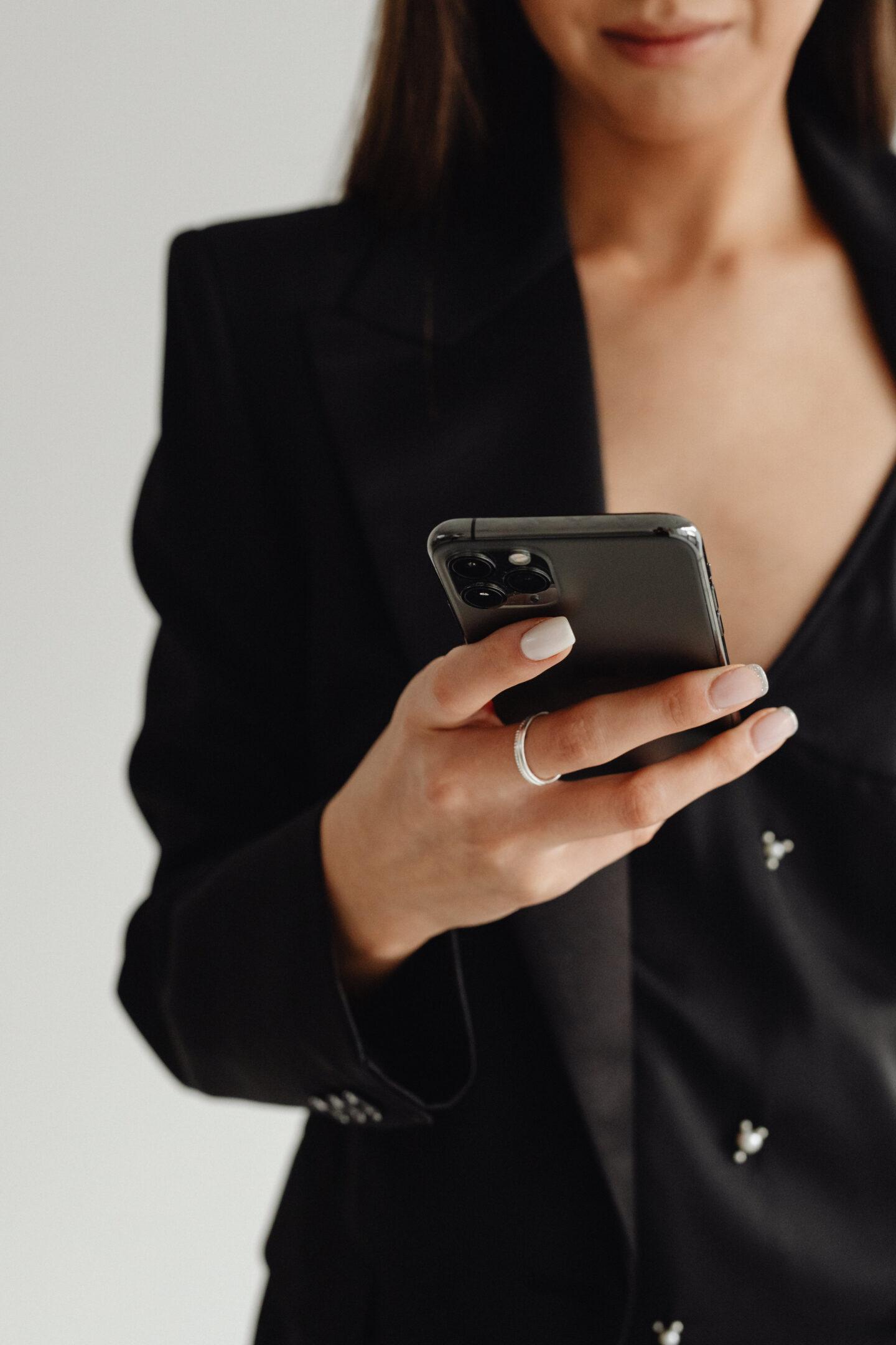 A woman dressed in a black blazer is holding a smartphone.