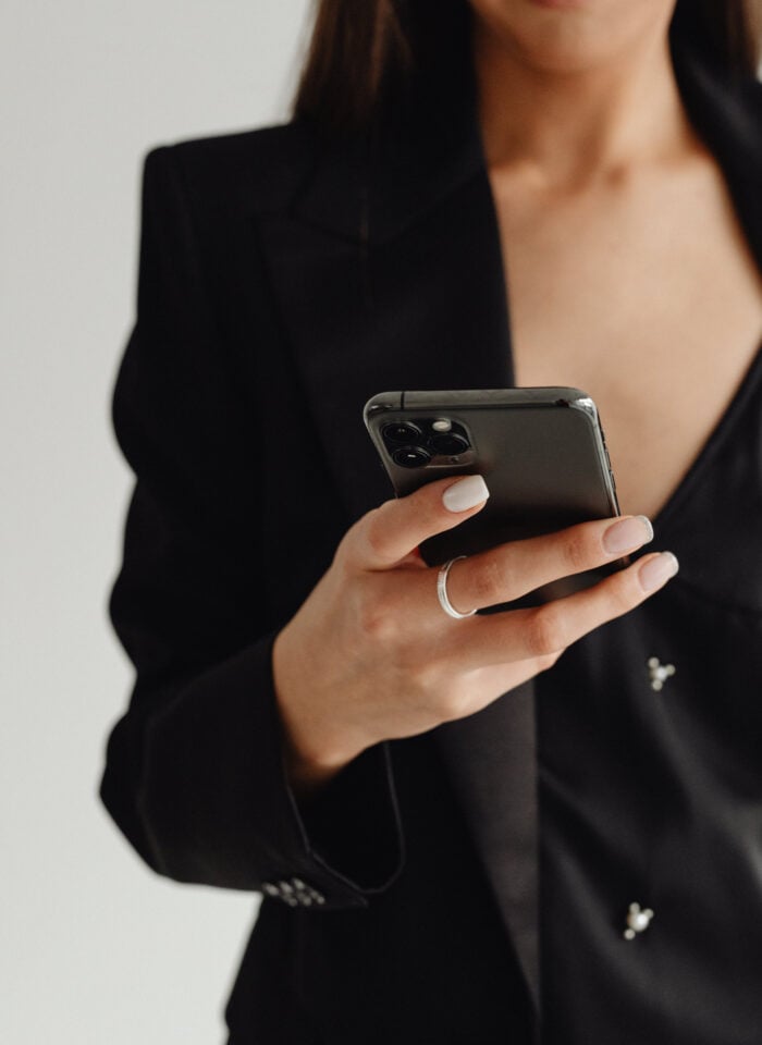 A woman dressed in a black blazer is holding a smartphone.