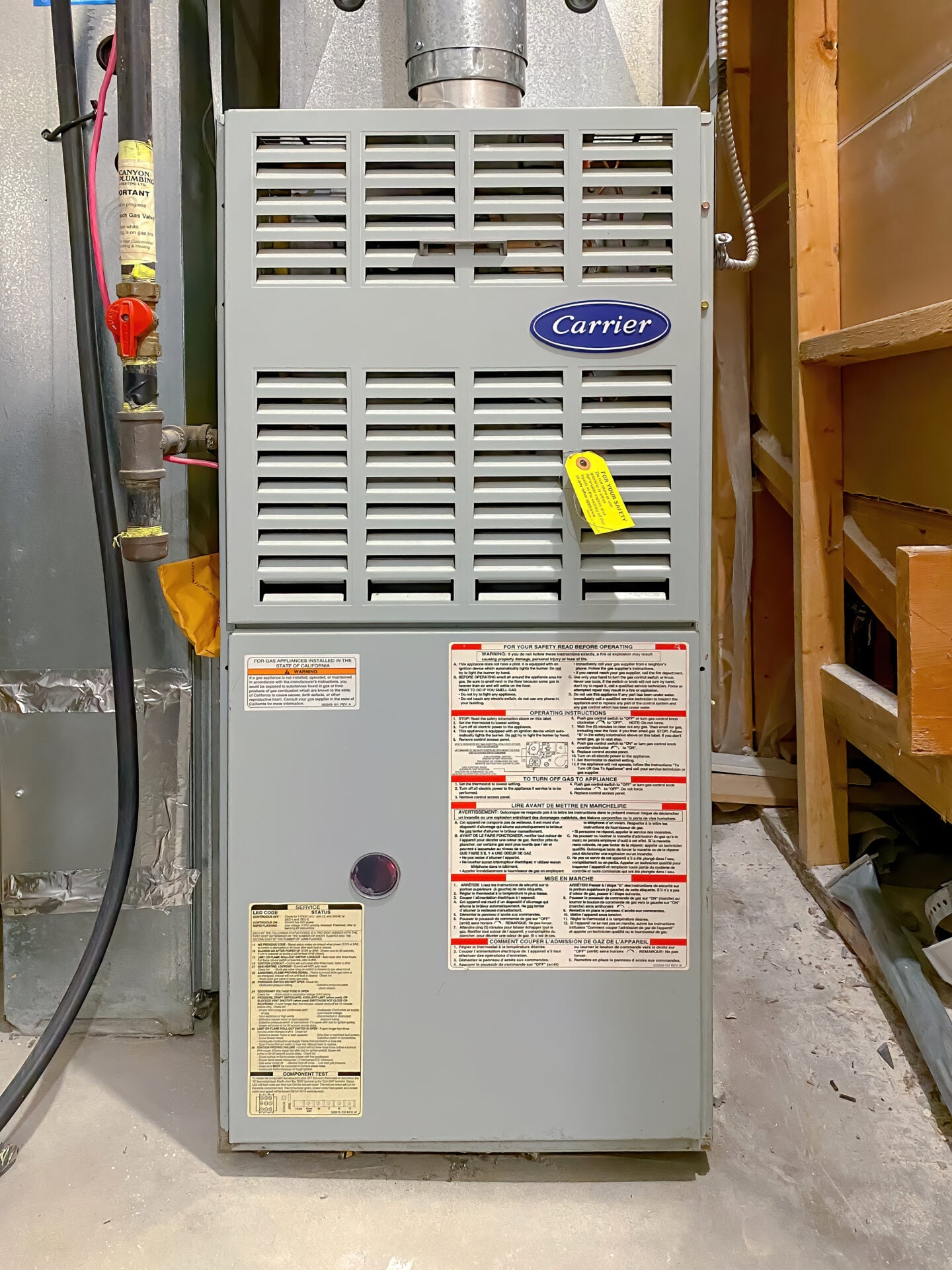 Carrier gas furnace unit installed in a basement, showing front panel with safety labels, vents, and connected piping.