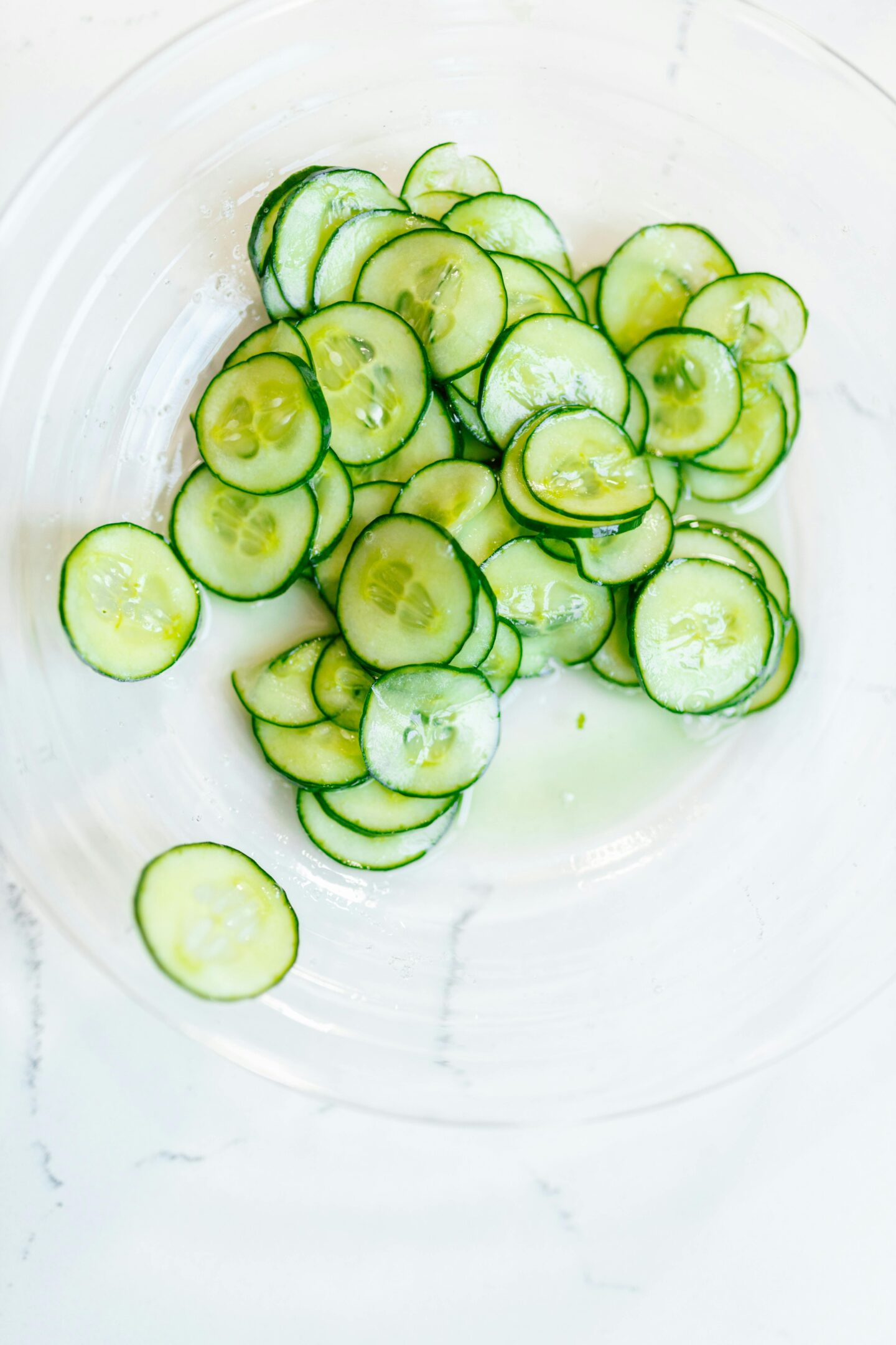 Fresh cucumber slices arranged in a clear glass bowl on a white surface.