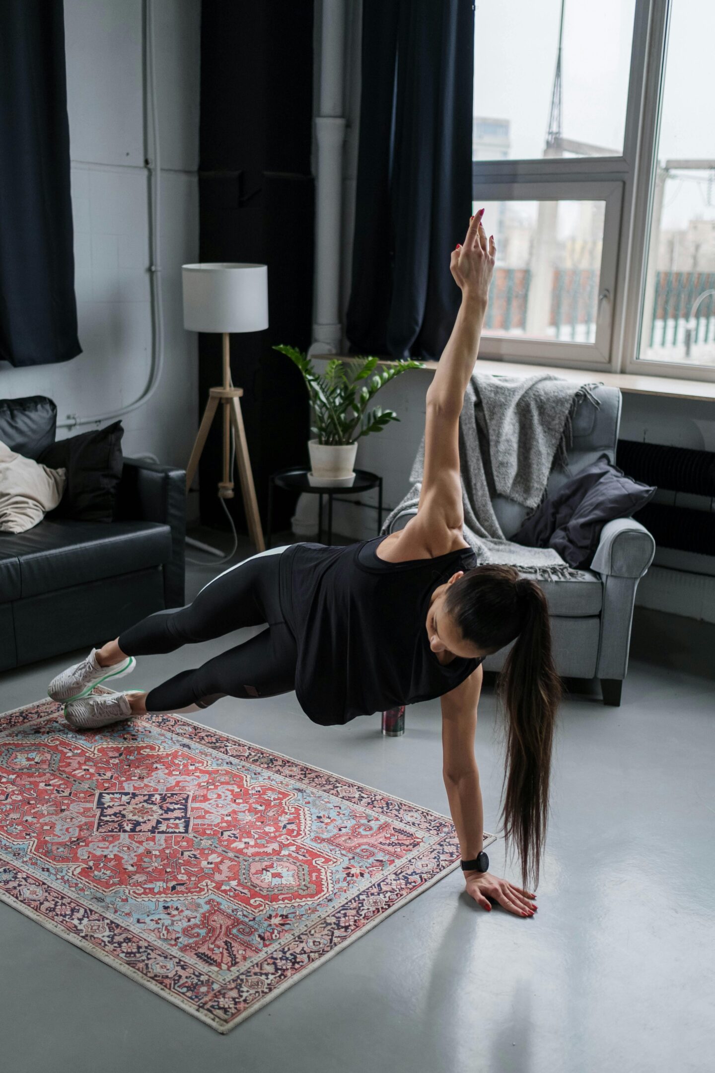 Woman exercising at home on a patterned rug, holding a side plank pose with one arm raised.
