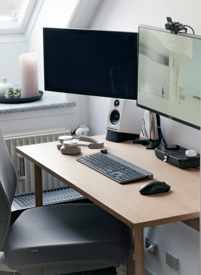Minimalist home office setup with dual monitors, wireless keyboard, mouse, and headphones on a light wood desk.