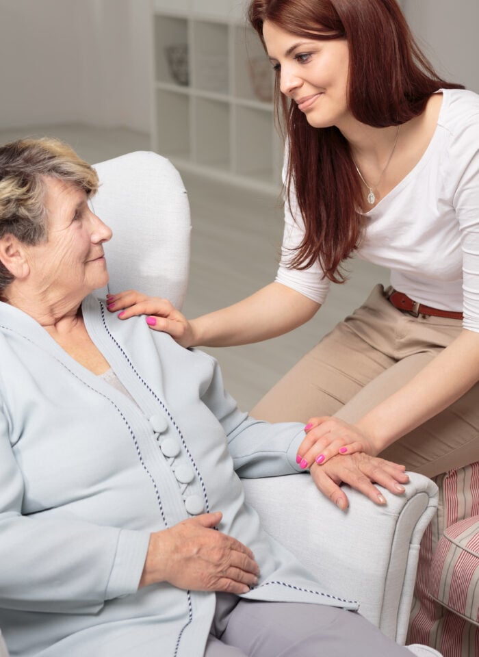 Friendly caregiver taking care of smiling senior woman during meeting at home