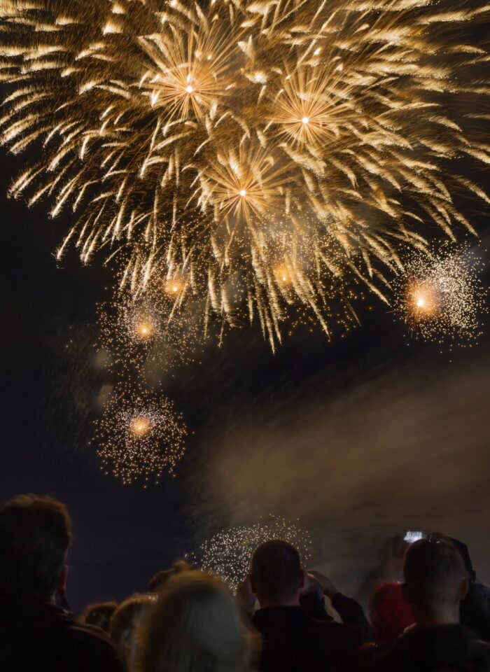 Crowds look up and take photos as golden fireworks burst across the dark night sky.