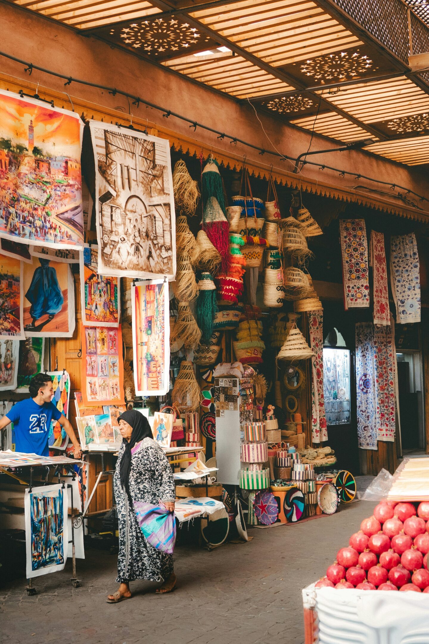 Vibrant market scene with woven baskets, textiles, and paintings displayed under patterned shade panels.
