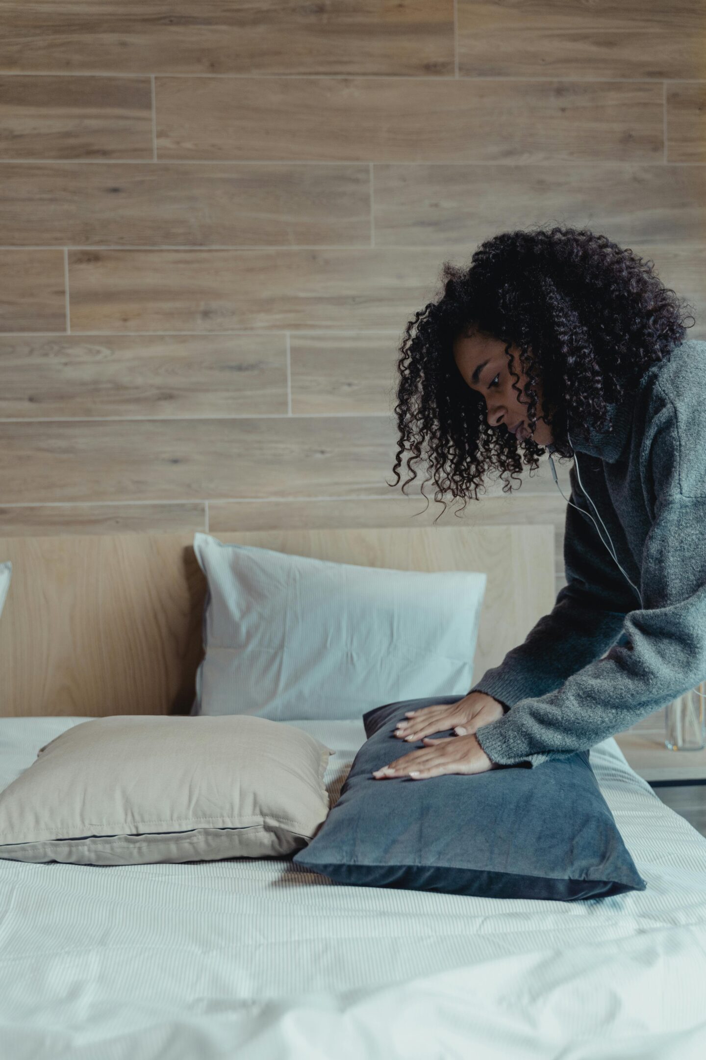 Woman arranging pillows while making a neatly dressed bed in a cozy bedroom.