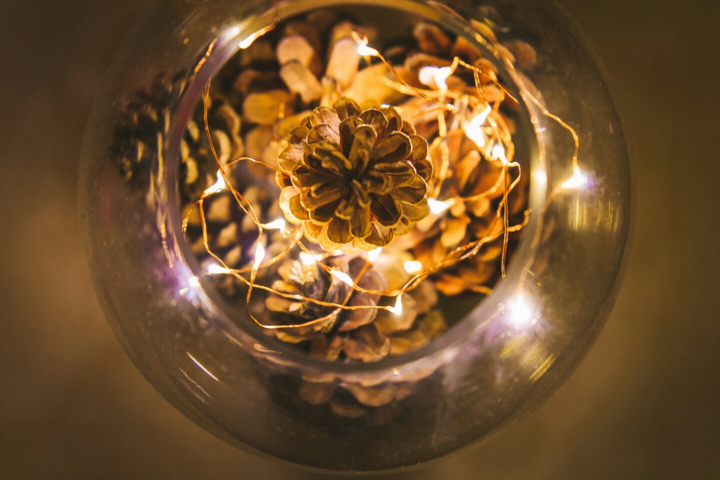 Glass bowl filled with pinecones and warm glowing string lights used as festive decor.