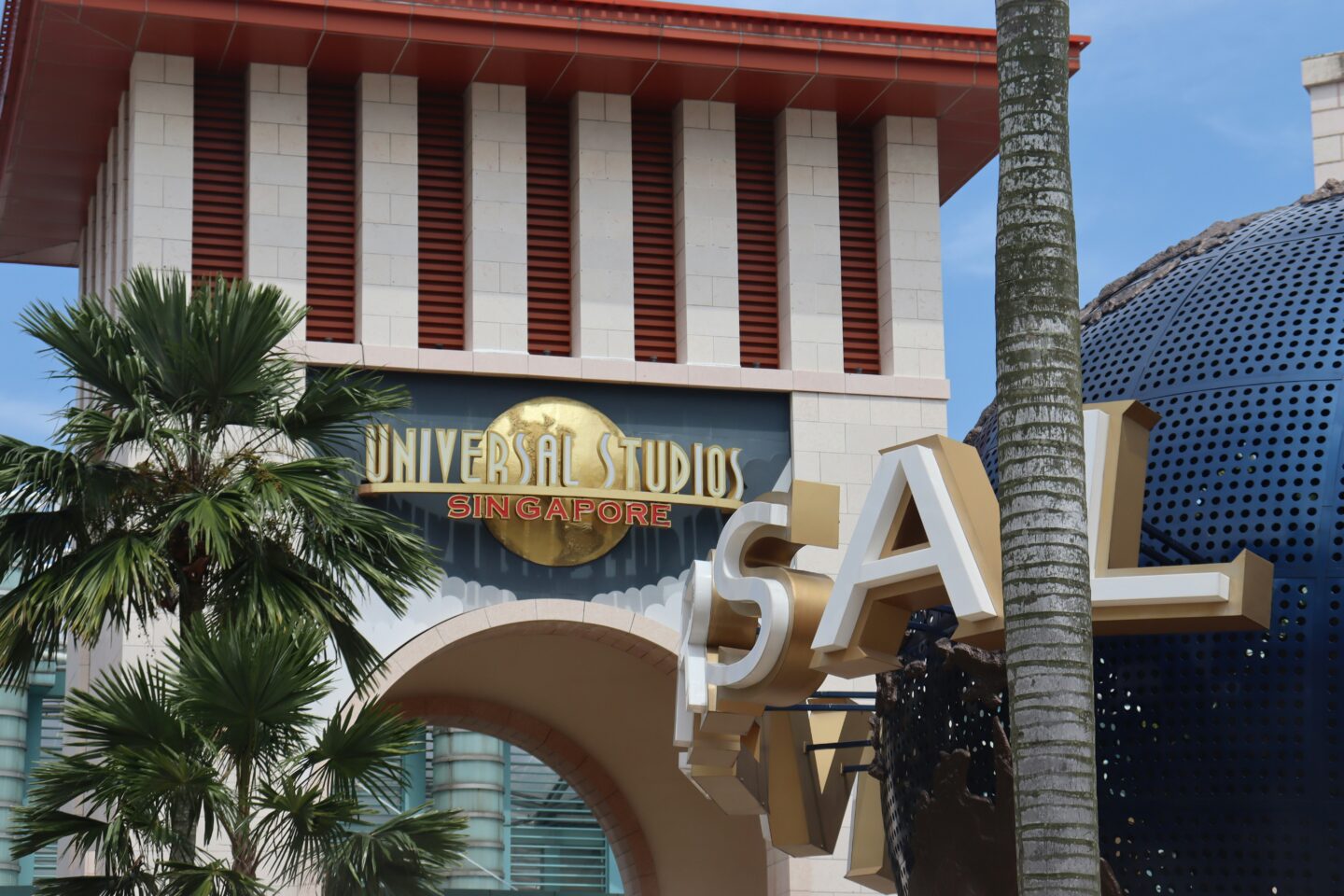 Entrance sign of Universal Studios Singapore with palm trees and architectural details in the background.