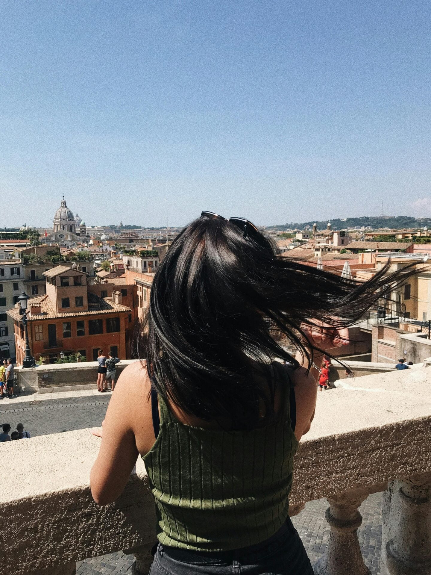 Woman in a green top looking out over the rooftops of Rome from a high viewpoint on a sunny day.