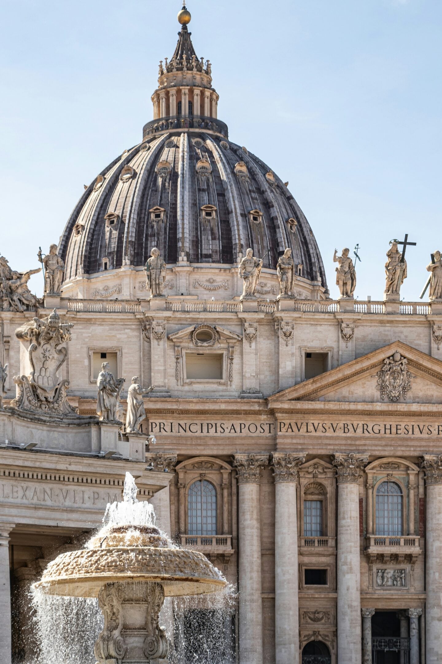 Close-up view of St. Peter’s Basilica dome and statues with a decorative fountain in the foreground in Vatican City.
