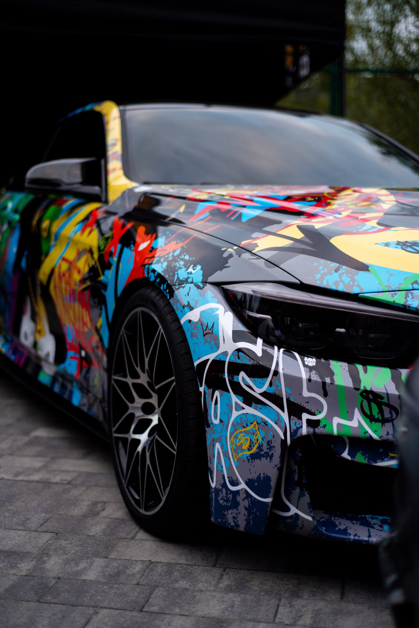 Sport car featuring a vibrant, multicolored graffiti-style wrap and large custom wheels.