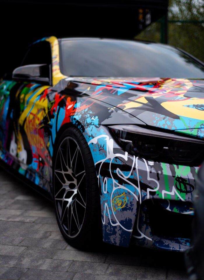 Sport car featuring a vibrant, multicolored graffiti-style wrap and large custom wheels.