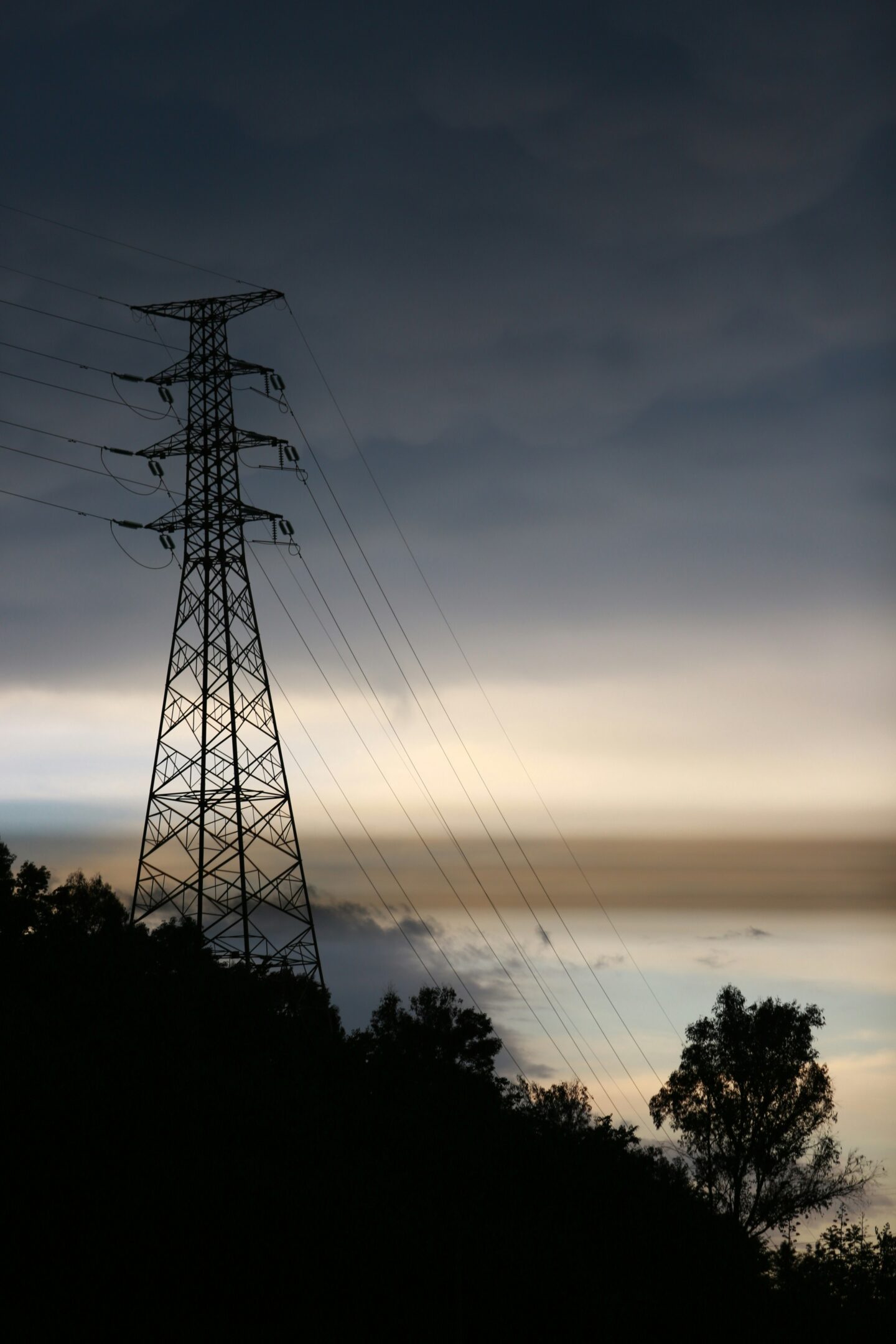 Electrical transmission tower and power lines silhouetted against a dramatic evening sky.