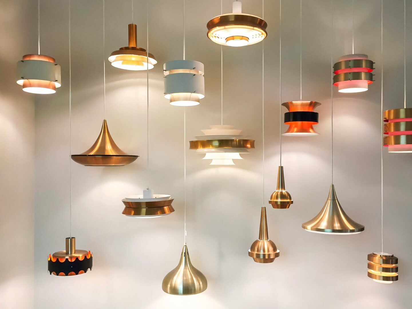 Collection of modern pendant lights in various metallic and white designs displayed on a wall.