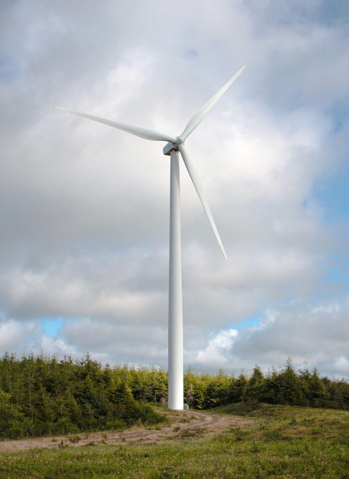 Large wind turbine standing in an open field with trees in the background under a cloudy sky.
