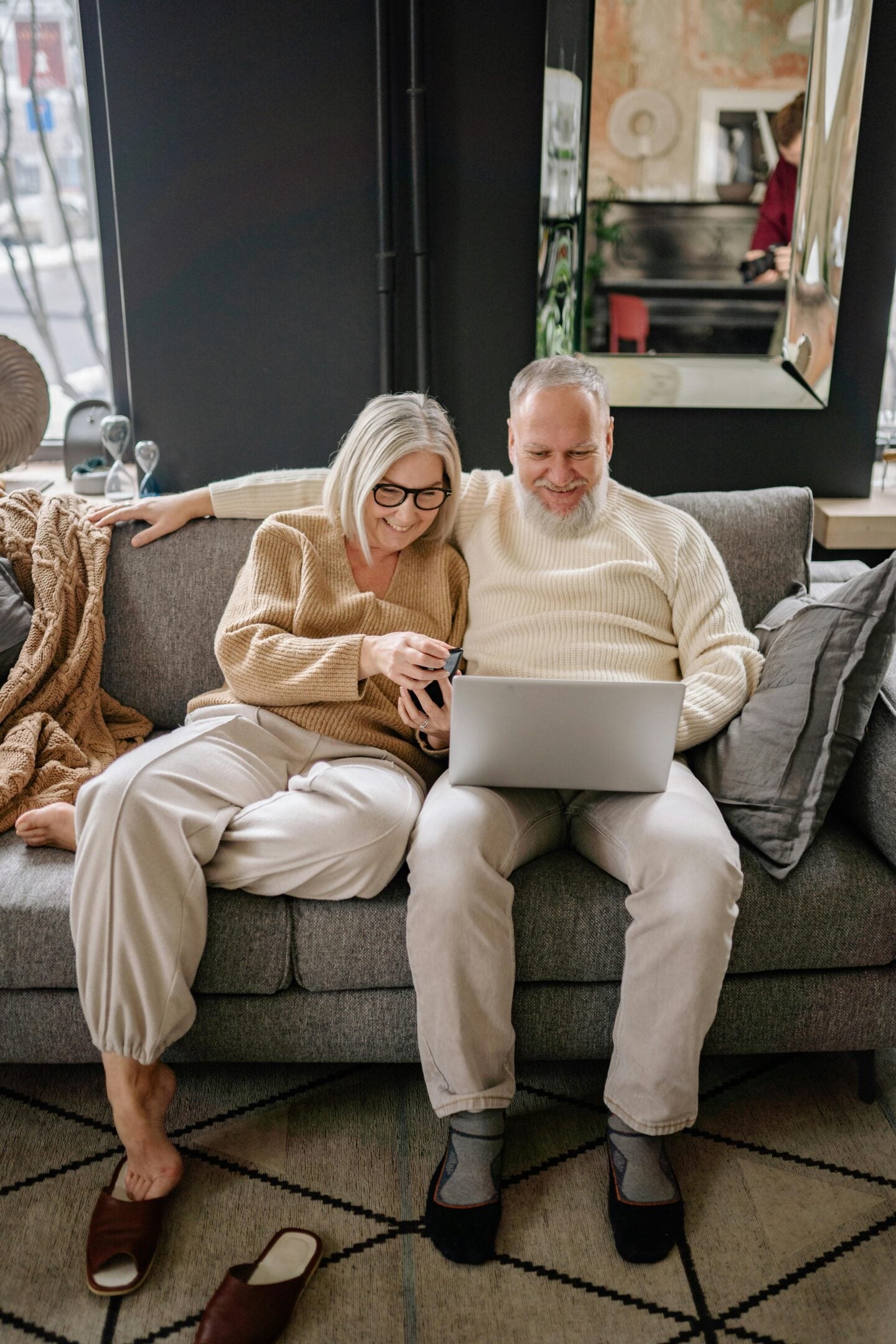 Smiling older couple sitting together on a sofa, looking at a laptop screen at home.