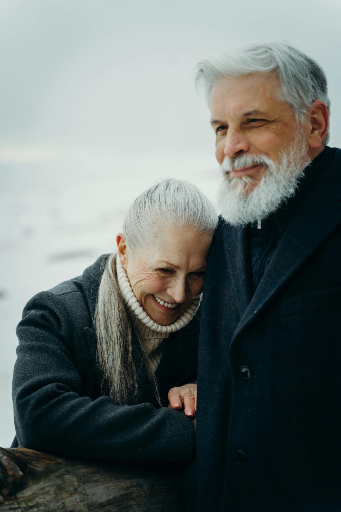 Older couple embracing outdoors on a cold day, smiling and enjoying each other’s company.