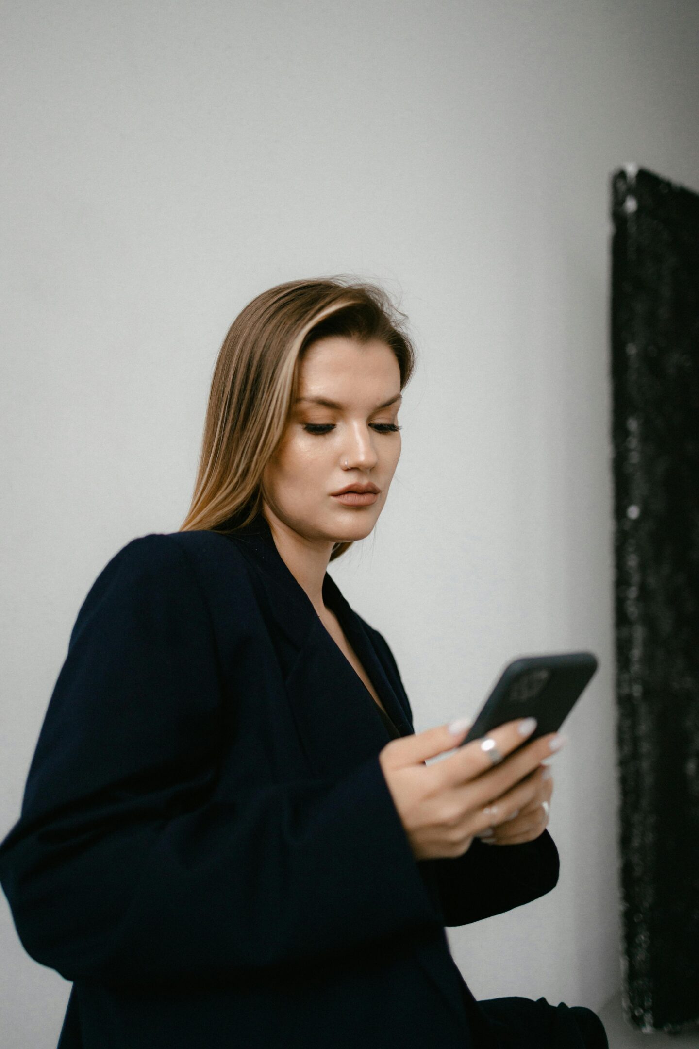 Woman wearing black smart blazer independently investing in stocks using a mobile trading app on her phone.