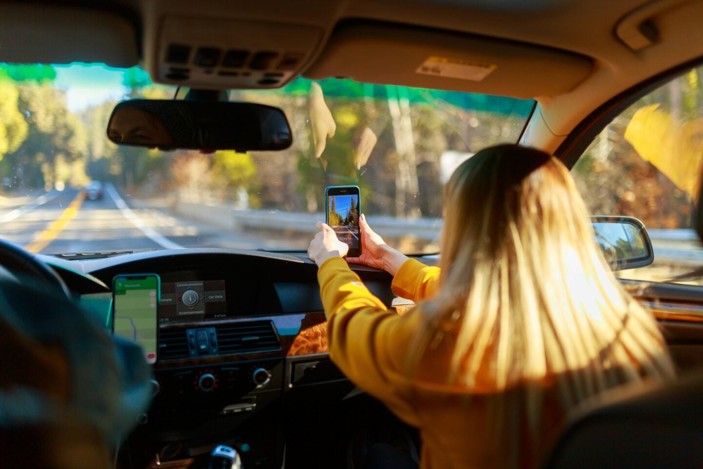 Passenger taking photos with a smartphone during a scenic family road trip through a forested highway
