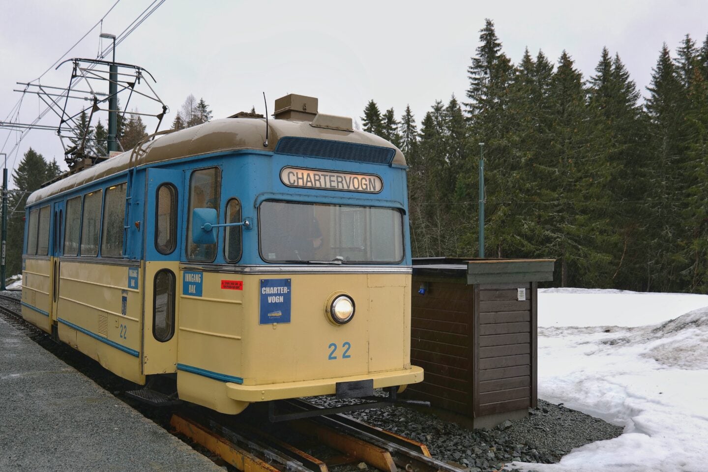 Historic tram at a snowy stop in Trondheim surrounded by forest, Norway