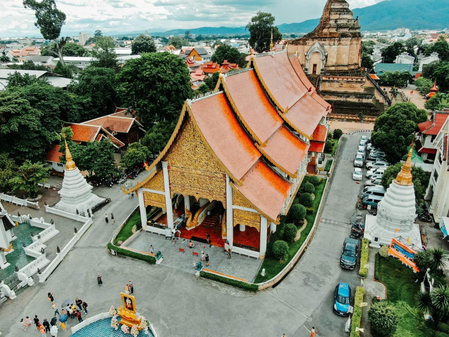 Aerial view of a traditional Thai temple complex in Chiang Mai, featuring ornate golden roofs, white stupas, and surrounding greenery.