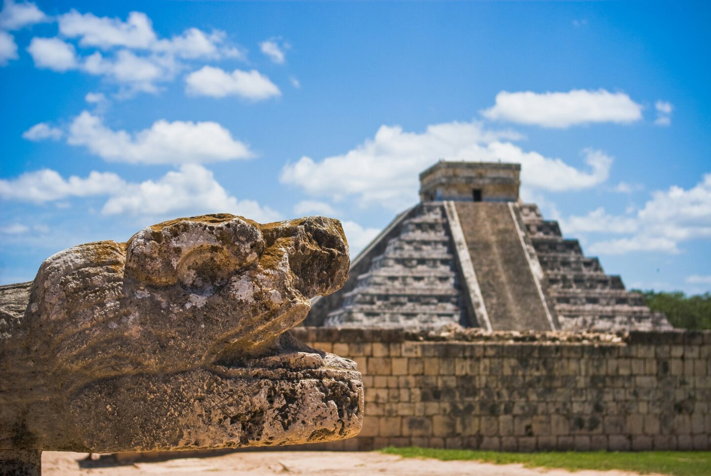 Stone serpent sculpture in the foreground with the El Castillo pyramid at Chichén Itzá near Mérida, Mexico.