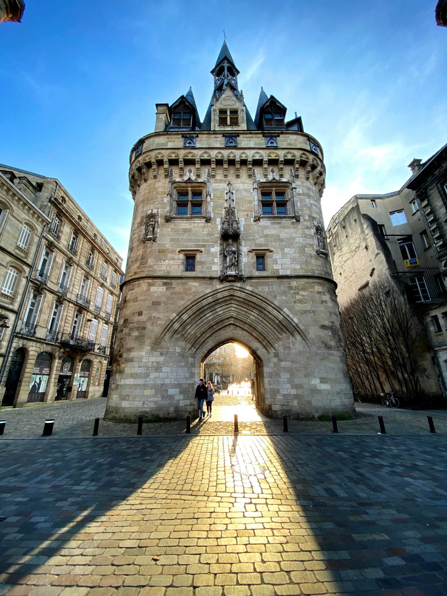 The medieval Porte Cailhau in Bordeaux, with sunlight streaming through its arched gateway onto the cobblestone square.