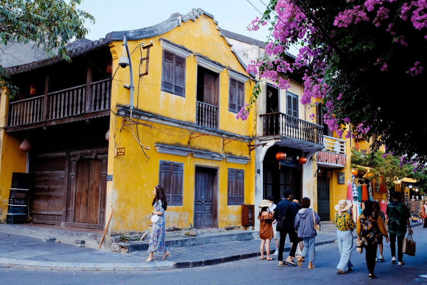 Yellow historic buildings and lantern-lit streets in Hoi An Old Town, Vietnam, with visitors walking past traditional shopfronts.