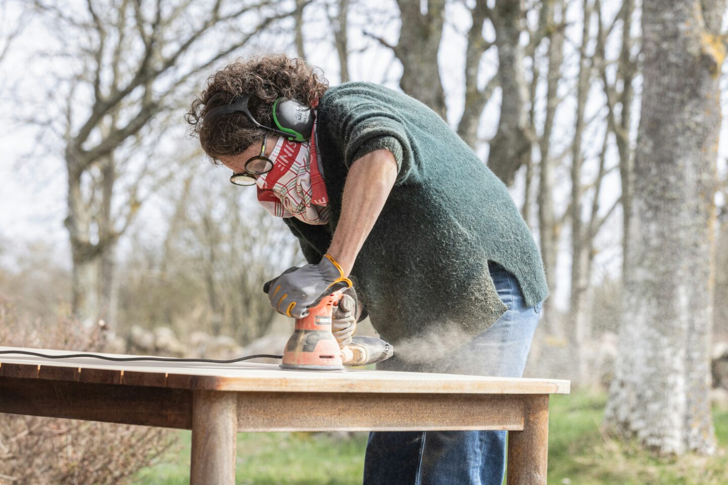 Person sanding a wooden table outdoors using tools, showing furniture repair and reuse
